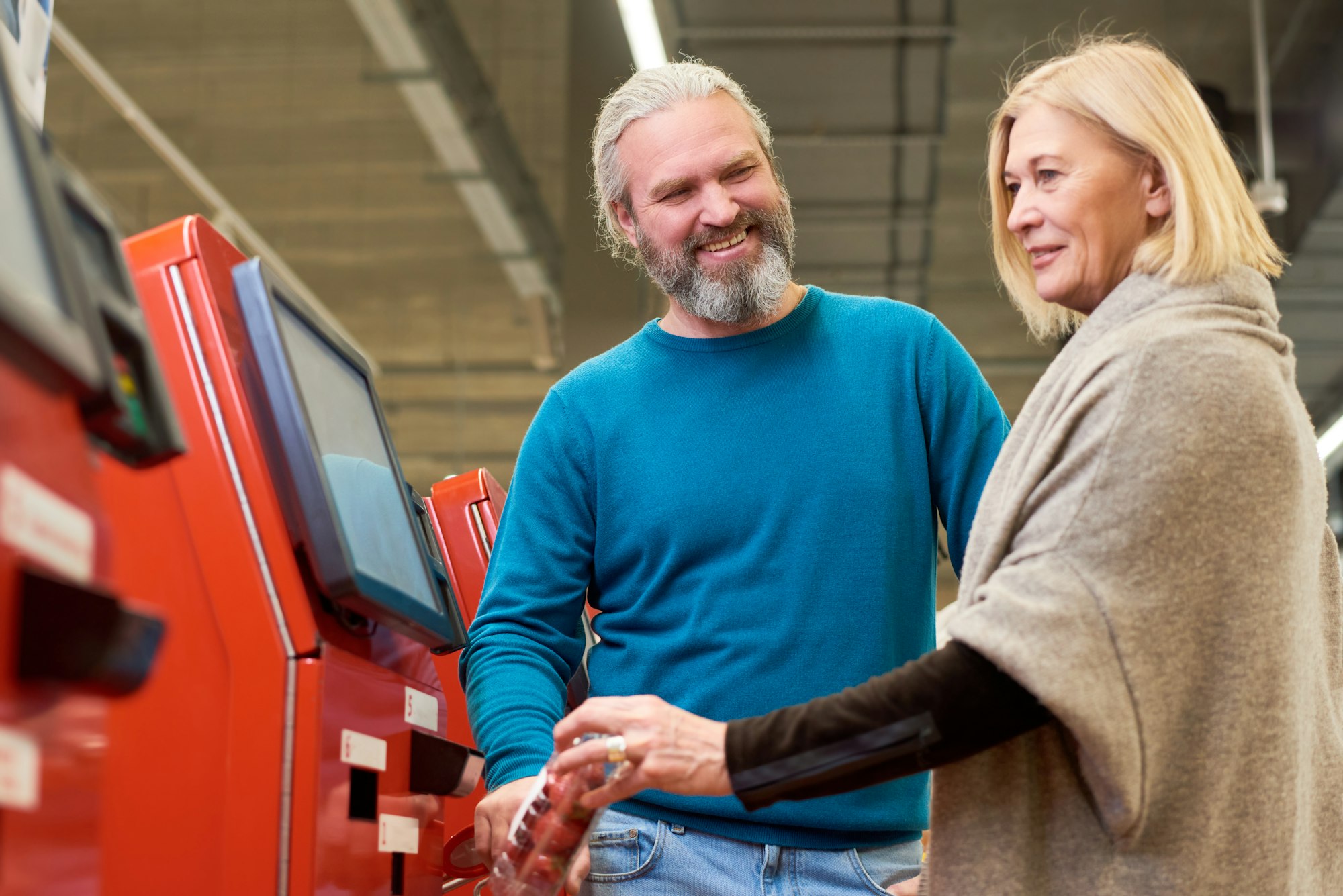 Happy aged man looking at his wife scanning packed fruits in terminal