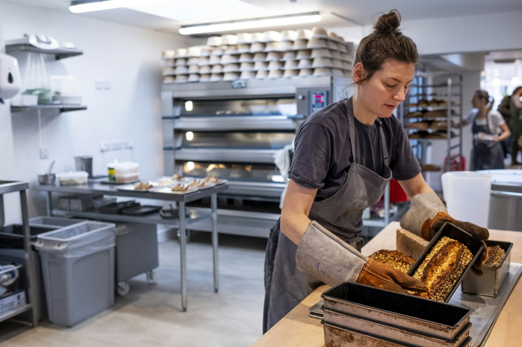 Woman wearing apron and oven gloves standing in an artisan bakery, turning out freshly baked loaves